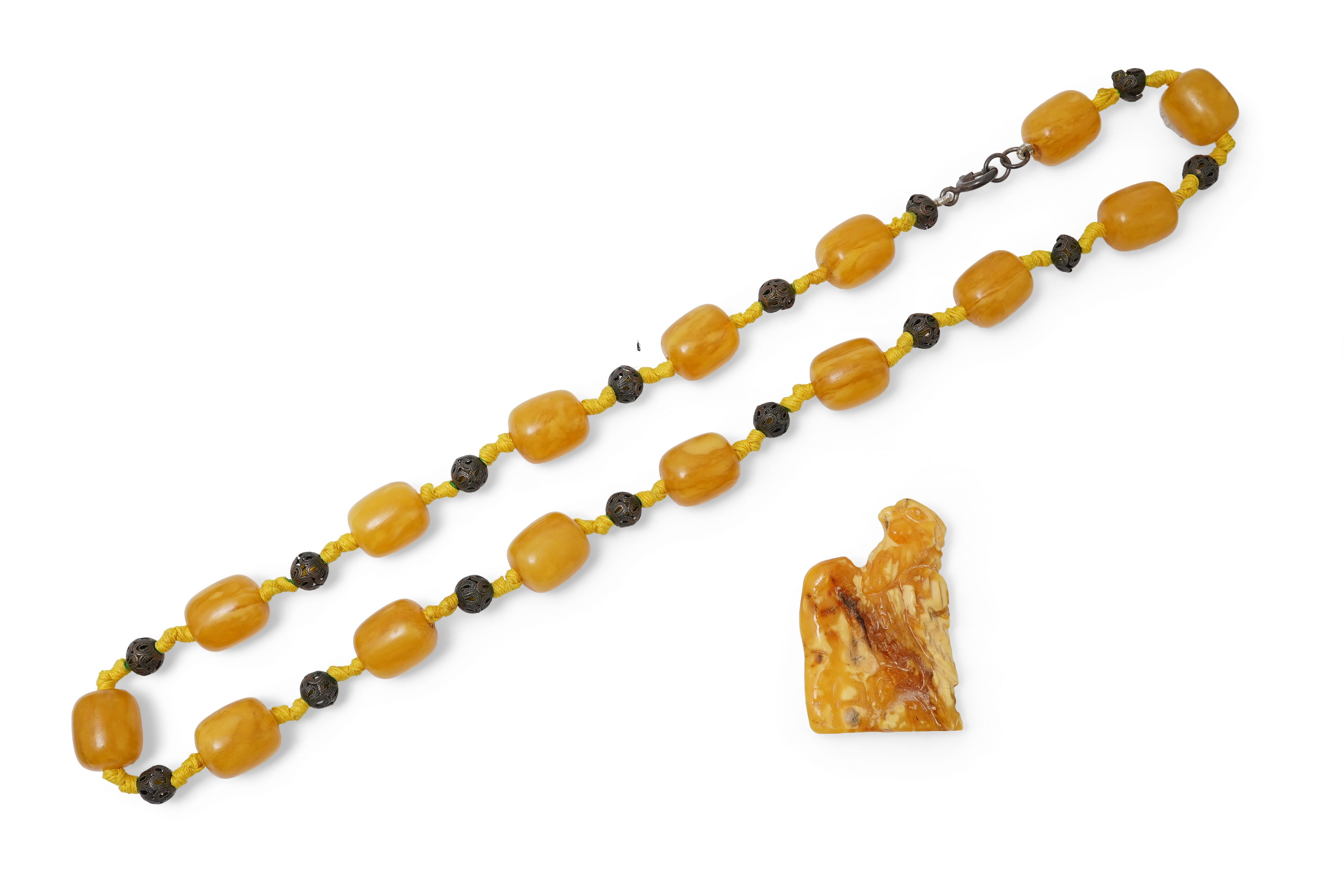 An amber necklace and carving, comprising: an amber necklace, composed of beads each measuring approximately 12 x 12 x 14mm, spaced by openwork metal beads, length 48cm; and an amber carving of a hawk on a rock, length 4